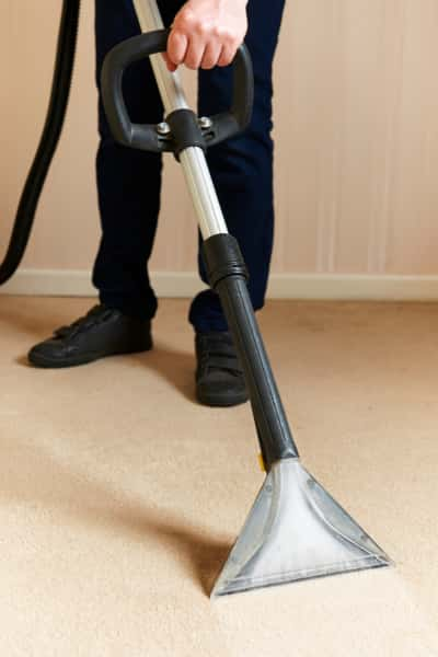 This is a photo of a man steam cleaning a cream carpet, using a professional steam cleaning machine works carried out by Clapham Carpet Cleaning Solutions