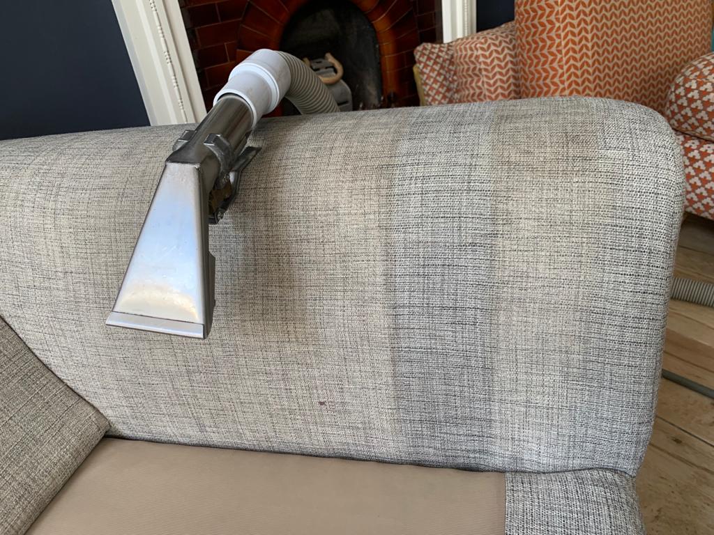 This is a photo of an arm of beige sofa that shows a test patch that has been steam cleaned. The steam cleaning machine is also showing in the photo works carried out by Clapham Carpet Cleaning Solutions